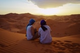 two men sitting on sand dunes