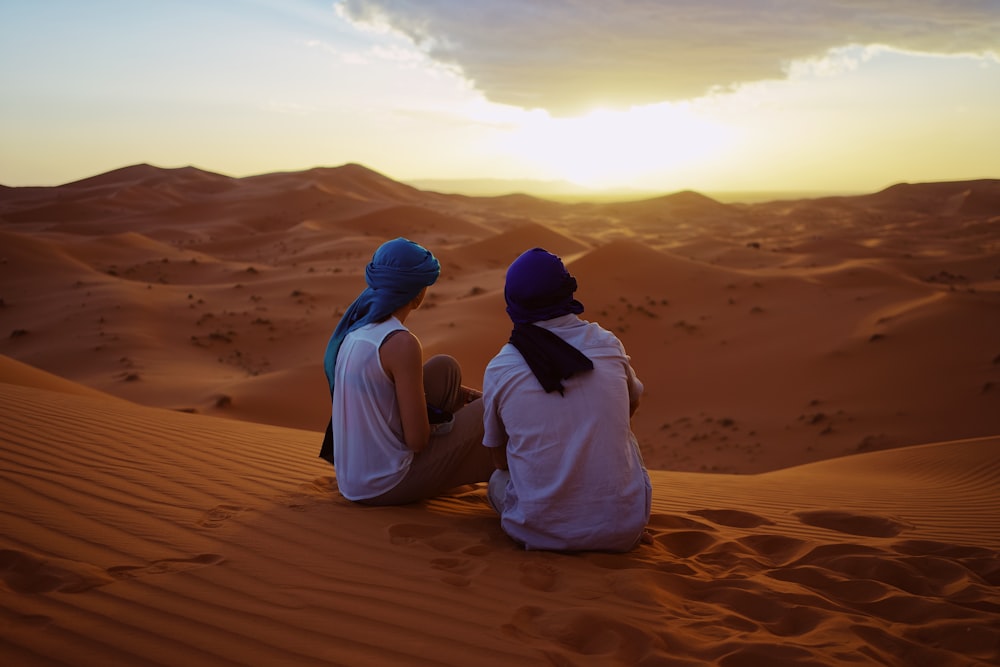 two men sitting on sand dunes