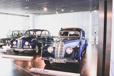A vintage European-style showroom with classic cars lined up under soft, muted lighting.