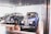 A collection of vintage cars is displayed in a sleek, modern showroom with large windows allowing natural light to illuminate the space. Two classic cars with polished, deep blue exteriors and chrome details are prominently featured, parked on elevated platforms.