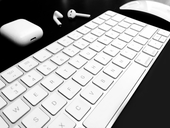 A sleek wireless headset resting beside a compact Bluetooth keyboard and mouse on a wooden desk.
