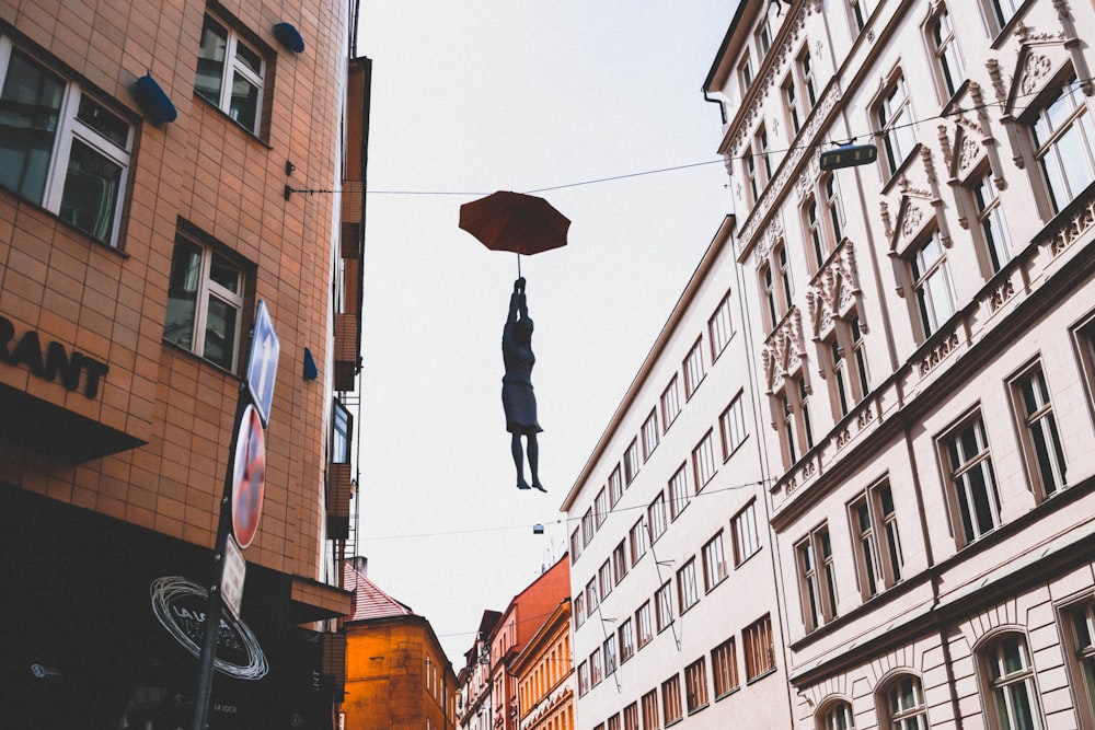 woman hanged on wire while holding umbrella between buildings at daytime