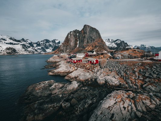 Red cabins on a rocky coastline beneath snow-capped mountains in Lofoten, Norway