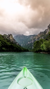 green kayak sailing near grass covered mountains during daytime