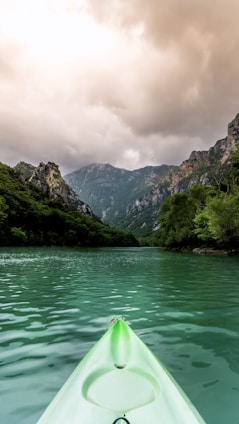green kayak sailing near grass covered mountains during daytime