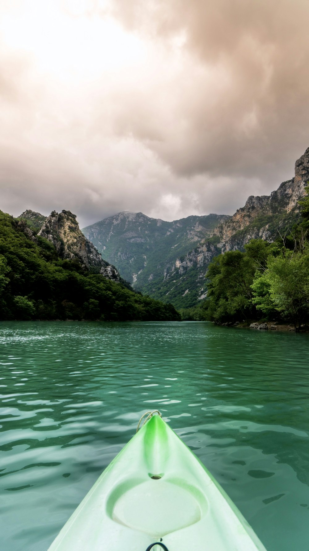 green kayak sailing near grass covered mountains during daytime