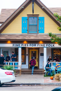 Smiling guests enjoying coffee and pie at a sunny outdoor event with the catering cart in the background.