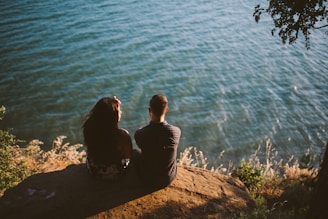couple sitting on rock near body of water
