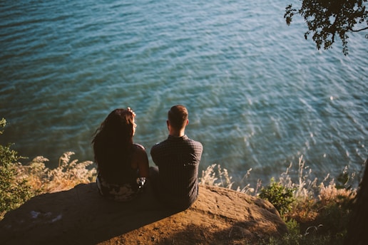 couple sitting on rock near body of water