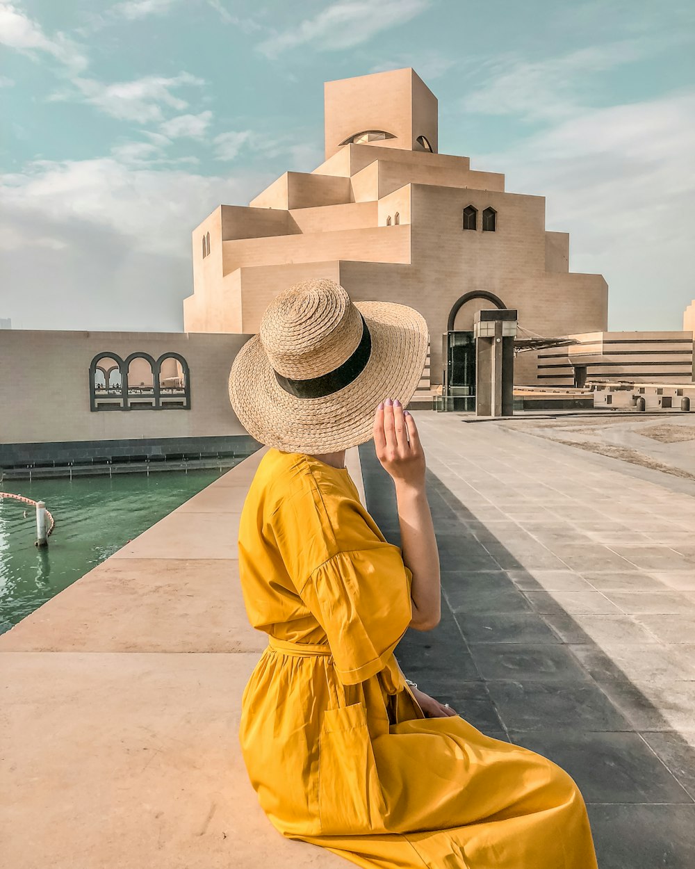 woman wearing sun hat and yellow dress in front of brown concrete building