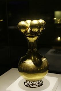 Luxurious black and gold churrigueresque vase displayed on a polished wooden pedestal.