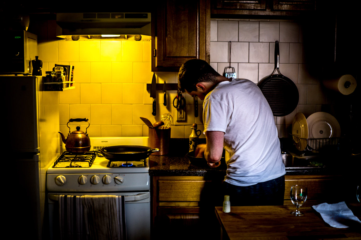 A person cooking at a stove in a kitchen lit yellow