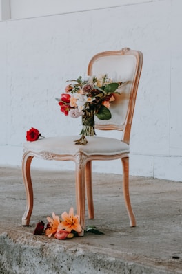 assorted-color flowers on brown wooden framed beige padded chair near wall