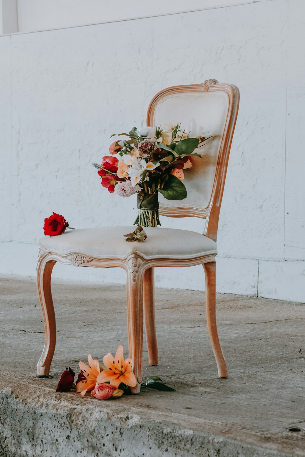 flores de colores variados en una silla acolchada beige con marco de madera marrón cerca de la pared