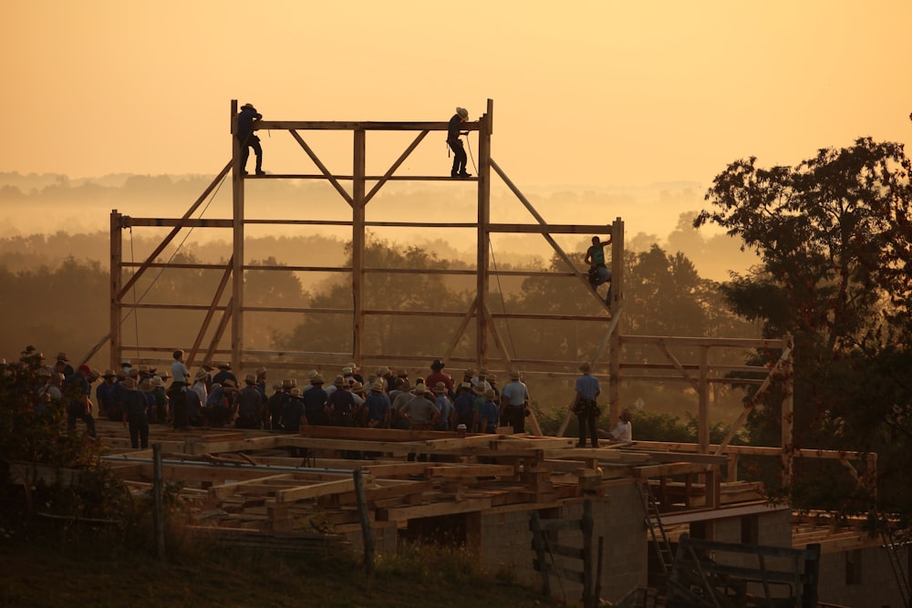 three person climbing a brown wooden housing frame