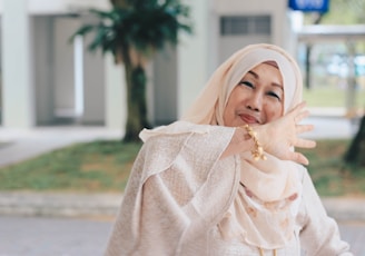 A woman wearing a solid color silk headscarf, smiling softly while walking through a sunlit park.