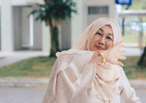 A woman wearing a solid color silk headscarf, smiling softly while walking through a sunlit park.