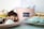 An assortment of desserts displayed on plates includes doughnuts with glaze and dried flowers, a cupcake with chocolate frosting, meringue cookies, and a cake slice. A box labeled 'Dolce Organico' holds more treats and is centrally positioned in the background.