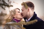 man and woman kissing near green leafed tree