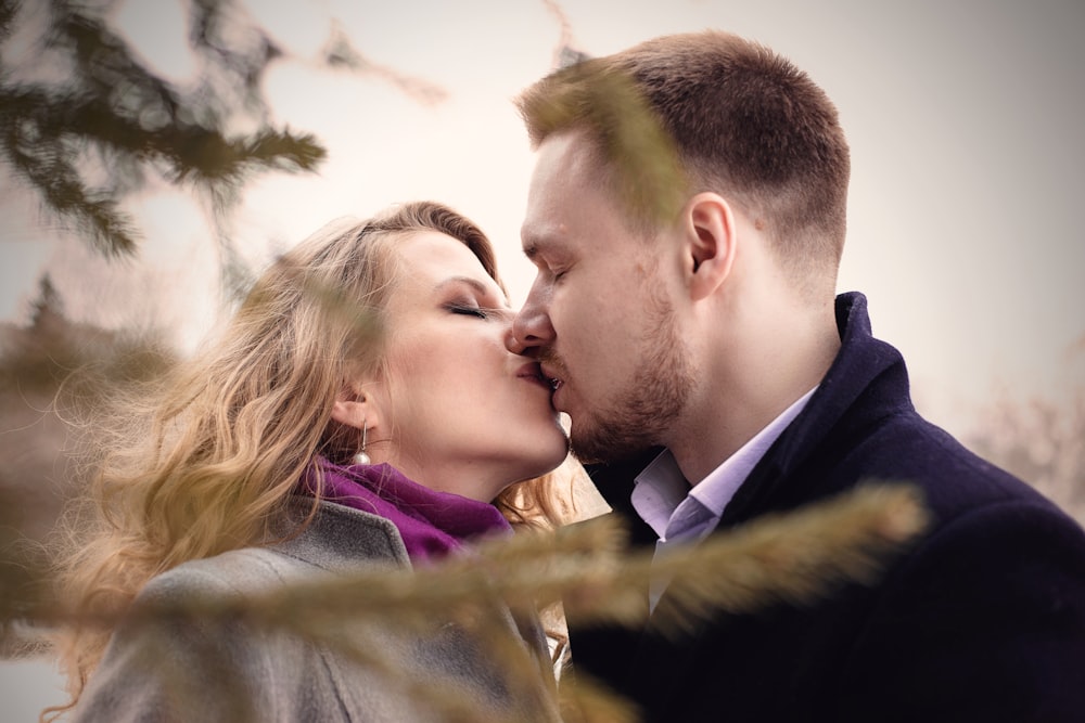 Mann und Frau küssen sich in der Nähe eines grünblättrigen Baumes