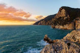 A dramatic shot of rocky cliffs meeting the deep blue sea at sunset.
