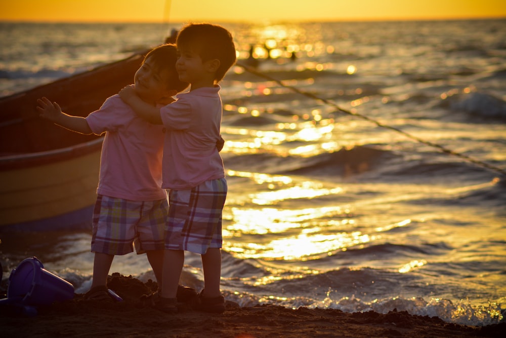 Dos niños de pie en la orilla del mar durante la puesta del sol