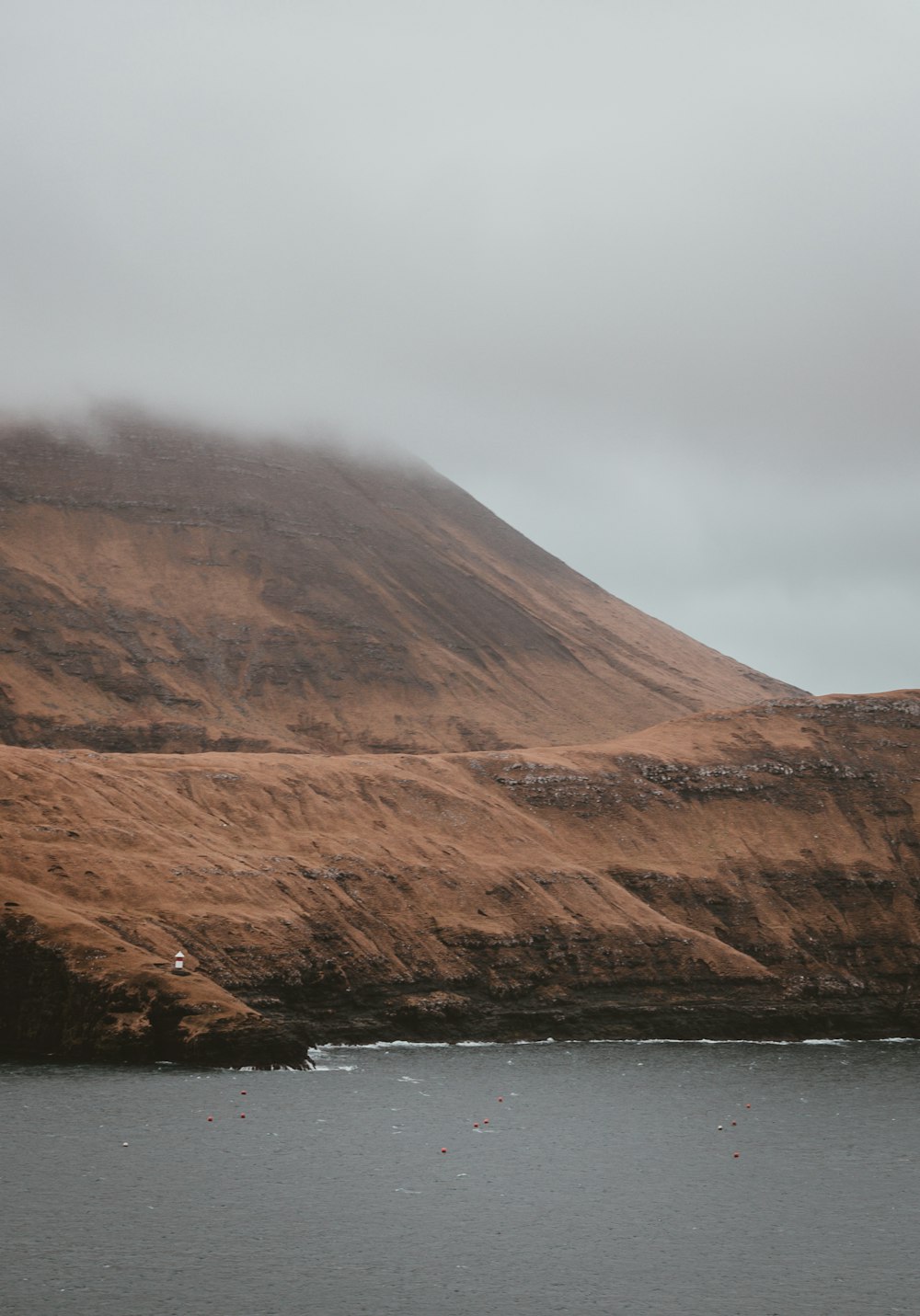 brown mountain near body of water under cloudy sky