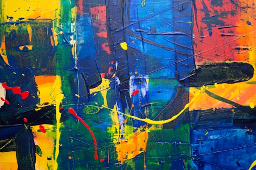 An abstract painting with bold, thick strokes of paint in vibrant colors, including blue, yellow, green, and red. The texture is rich with layers of paint that create a dynamic, energetic composition. Random splashes and drips contribute to the abstract nature, giving a sense of movement.