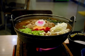 A steaming pot of soup on a stove with fresh ingredients nearby