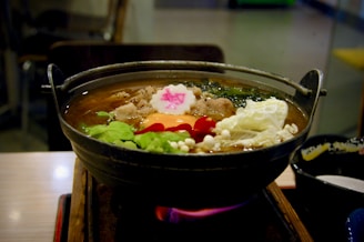 A steaming pot of soup on a stove with fresh ingredients nearby
