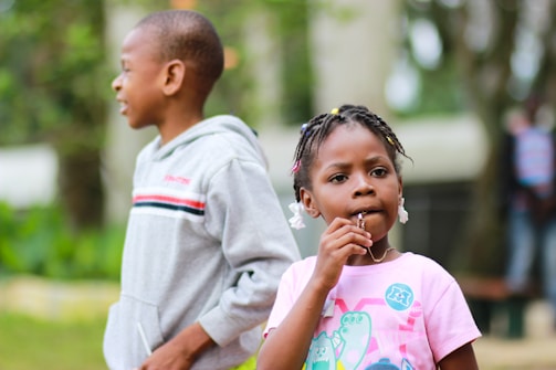 selective focus photography of girl biting her pendant beside a boy in gray pullover hoodie