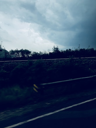 A sturdy transport truck moving steadily along a highway under a cloudy sky.
