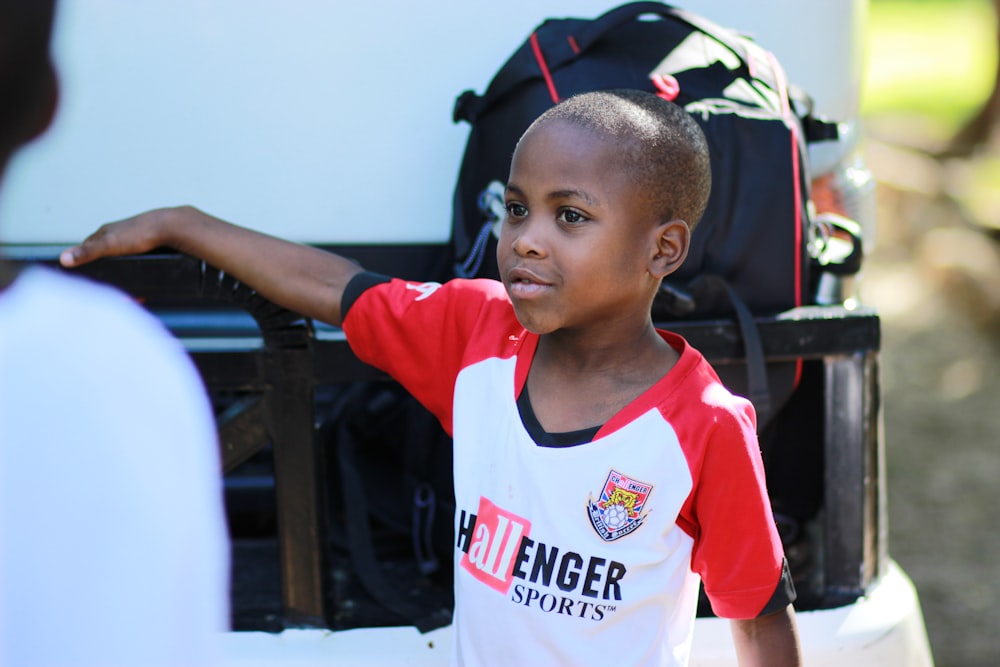 boy in white and red V-neck shirt in front of black backpack