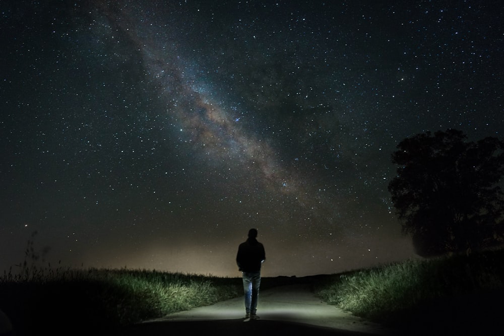 夜、星空の下、緑の芝生の間のコンクリートの道を歩く男