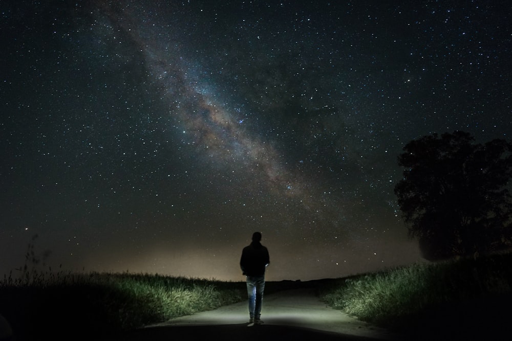 hombre caminando en camino de cemento entre la hierba verde bajo el cielo estrellado durante la noche