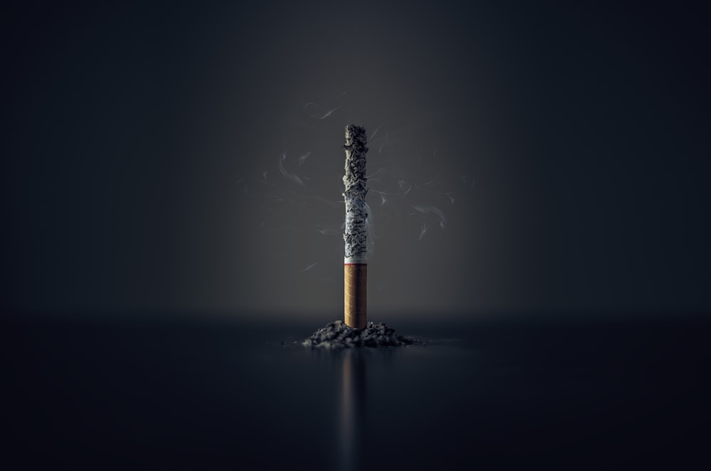 single cigarette of unspecified type burning, with pile of ashes around it.