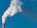 A chimney releasing a large plume of white smoke against a clear blue sky. The smoke appears thick and voluminous, suggesting industrial activity.