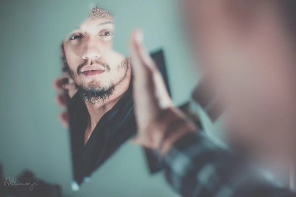 A man looking at his reflection in a mirror, adjusting his jacket