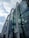 A modern glass building features large, curved arches that create a distinctive architectural design. The building's reflective glass panels mirror the cloudy sky and surrounding environment, adding depth and dynamism to the structure.