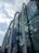 A modern glass building features large, curved arches that create a distinctive architectural design. The building's reflective glass panels mirror the cloudy sky and surrounding environment, adding depth and dynamism to the structure.