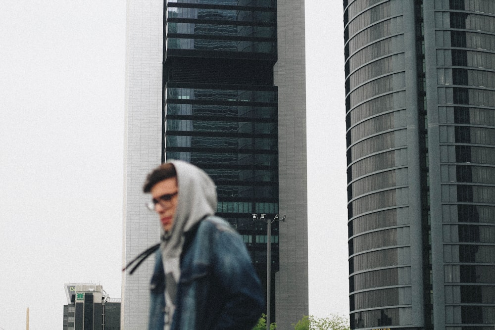 高い建物の前を歩くパーカーを着た男