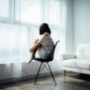 woman sitting on black chair in front of glass-panel window with white curtains