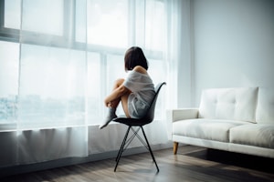 woman sitting on black chair in front of glass-panel window with white curtains