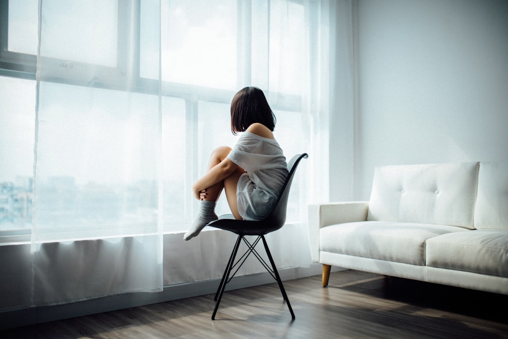 Frau sitzt auf schwarzem Stuhl vor Glasfenster mit weißen Vorhängen
