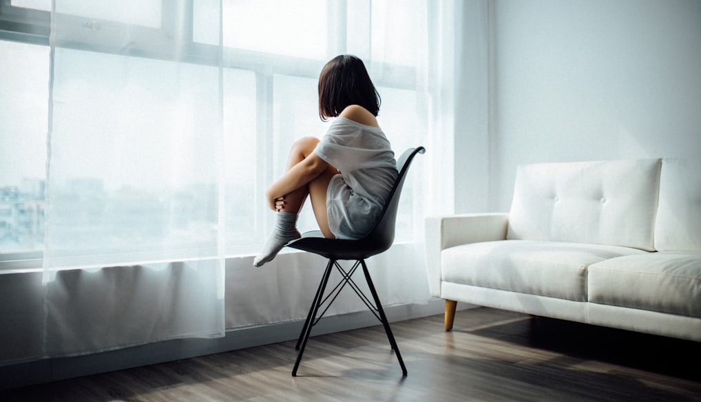 woman sitting on black chair in front of glass-panel window with white curtains