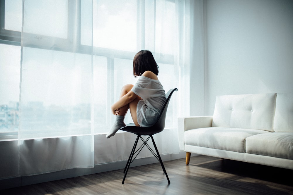 woman sitting on black chair in front of glass-panel window with white curtains