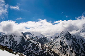 Snow-capped mountains under a clear blue sky with fluffy white clouds