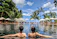 Smiling woman relaxing by a luxury resort pool with palm trees in the background.
