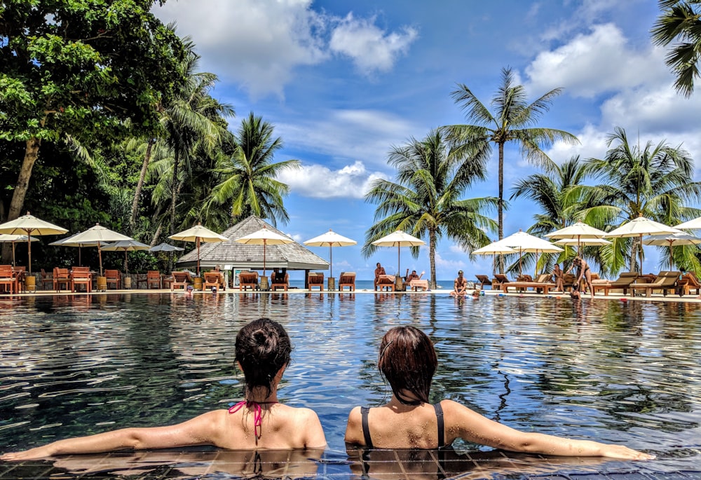 two woman leaning on inground pool tile