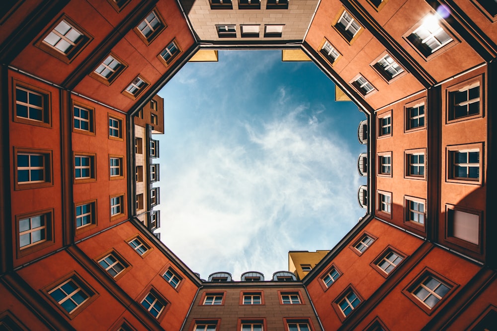 low-angle photography of hexgonal orange and brown concrete building under white clouds and blue sky during daytime